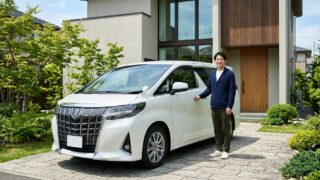 パールホワイトのアルファード2.5Zグレードの横に立ち笑顔を見せる若い日本人男性