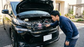 ヴェルファイアのボンネットを開けてラジエーター周辺のピンク色の水漏れ結晶を点検する若い日本人男性オーナー