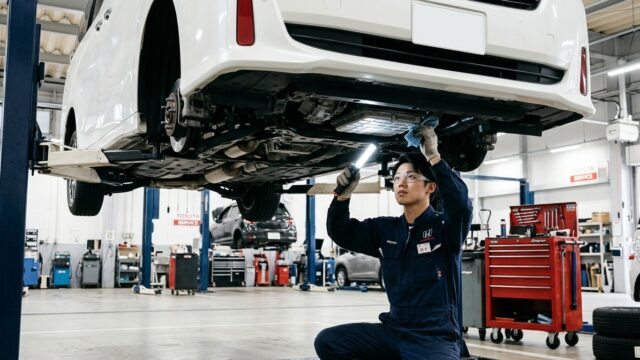 清潔な日本の自動車整備工場でリフトアップされたヴェルファイアの下回りとCVTオイルパンを点検する若い日本人男性整備士